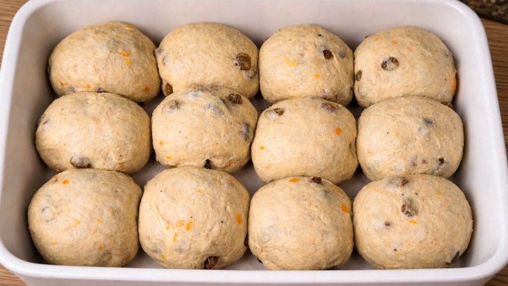 Soft and fluffy Hot Cross Buns – dough shaped into smooth round balls and neatly arranged on a baking tray lined with parchment paper, ready for the final rise before baking.