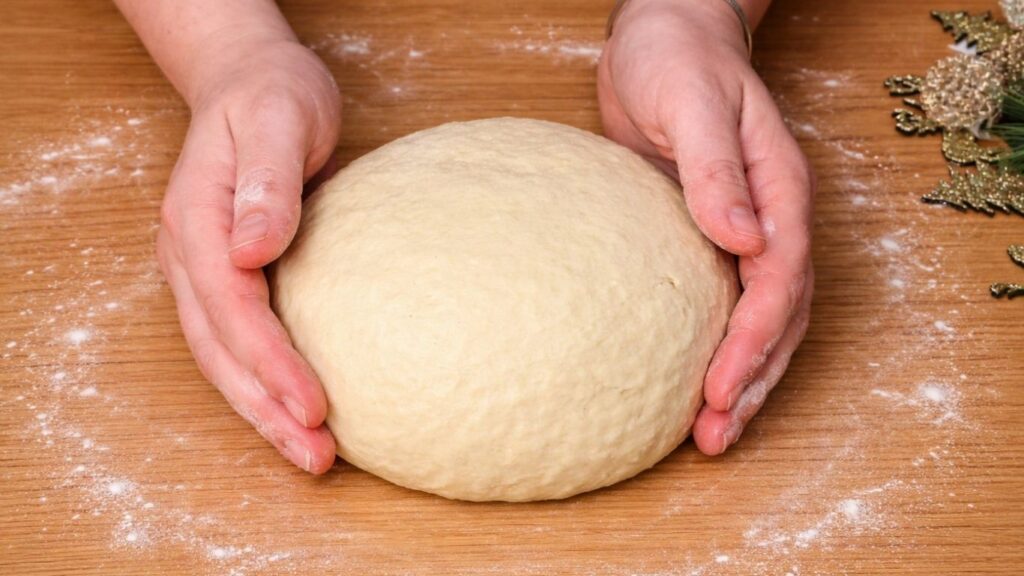 Kneading the dough on a wooden work surface and shaping it into a smooth ball, ready for the first rise for soft and fluffy chocolate swirl buns.