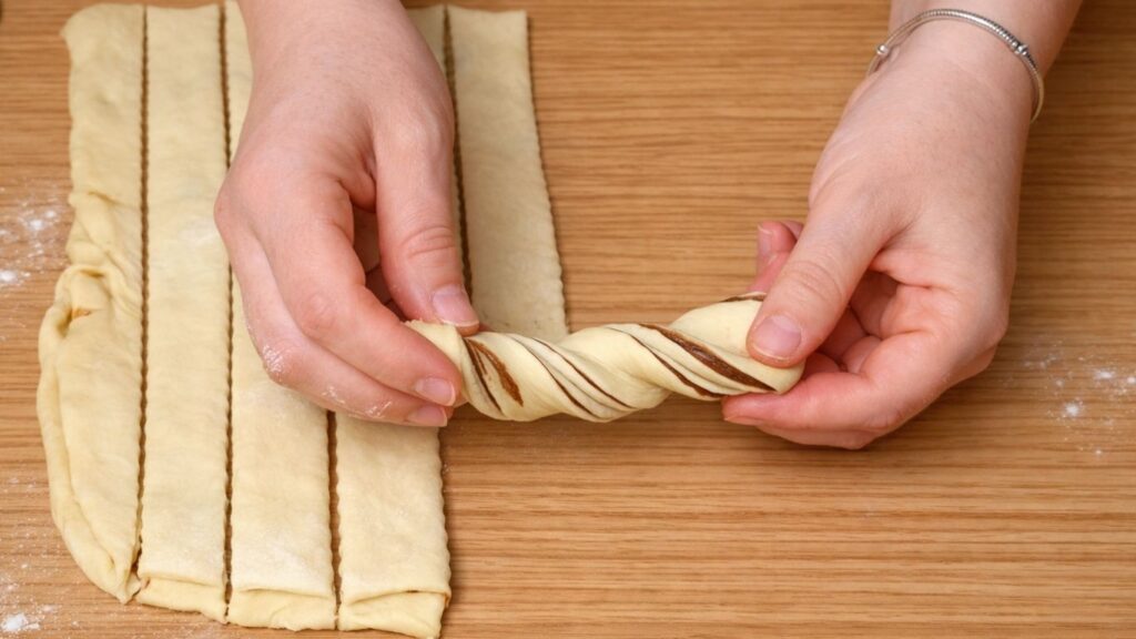 Strips of dough twisted into spiral shapes, ready to be formed into chocolate swirl buns before baking.