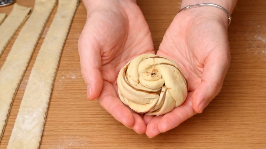 Shaped chocolate swirl bun held in hands, showing the twisted spiral layers of dough before proofing and baking.