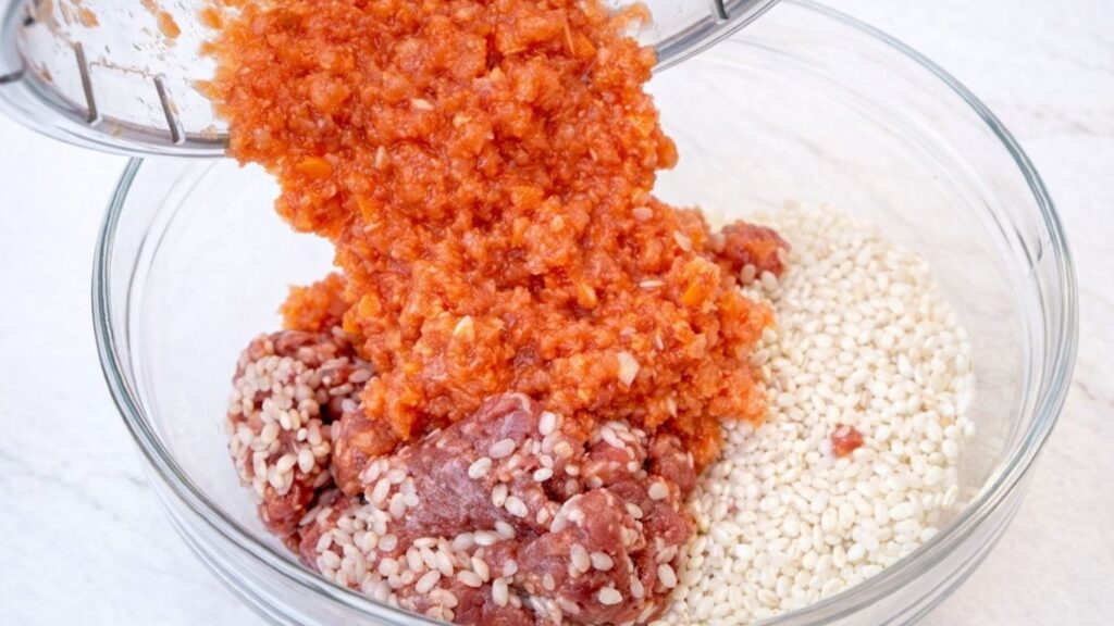 Pouring blended vegetables into a bowl with ground meat and rice, preparing the filling mixture for traditional sarma stuffed cabbage rolls