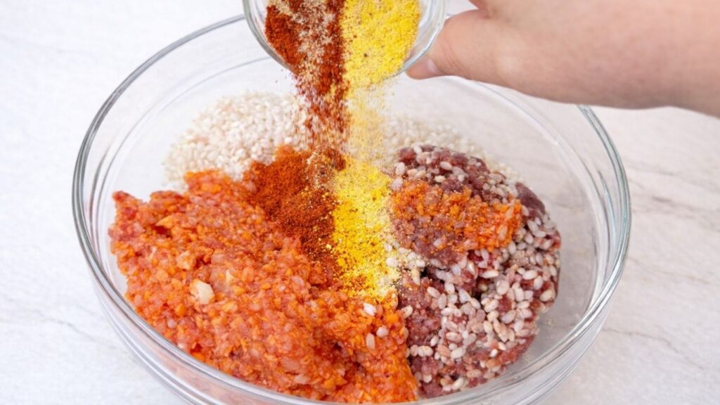 Adding spices to a bowl with ground meat, rice, and vegetables, preparing the seasoned filling for traditional sarma stuffed cabbage rolls