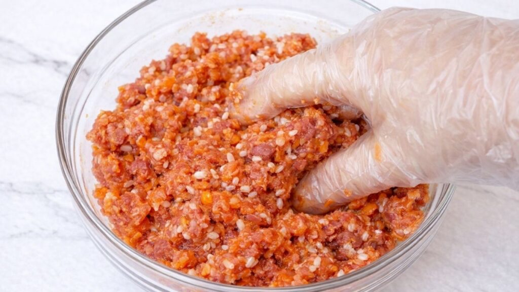 Alt text:
Mixing the sarma filling by hand with a glove, combining ground meat, rice, vegetables, and spices into a well-blended mixture for stuffed cabbage rolls