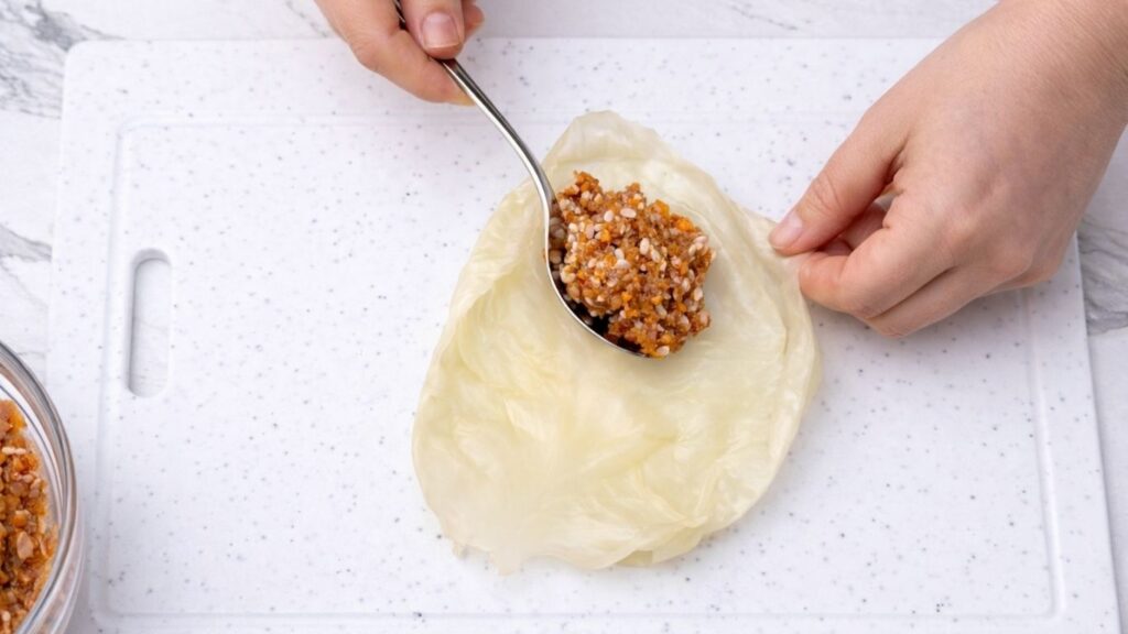 Placing a spoonful of meat and rice filling onto a sour cabbage leaf, preparing to roll traditional sarma stuffed cabbage rolls