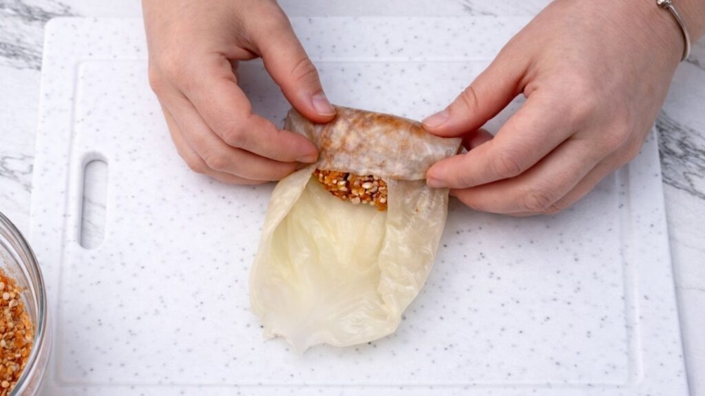 Folding the sides and bottom of a sour cabbage leaf over the meat and rice filling, shaping it into a tight roll for traditional sarma stuffed cabbage rolls