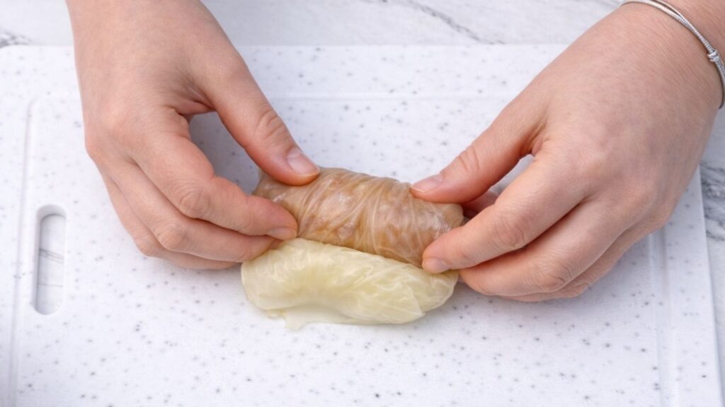 Rolling the cabbage leaf all the way to the end, forming a finished sarma roll filled with meat and rice for traditional stuffed cabbage rolls