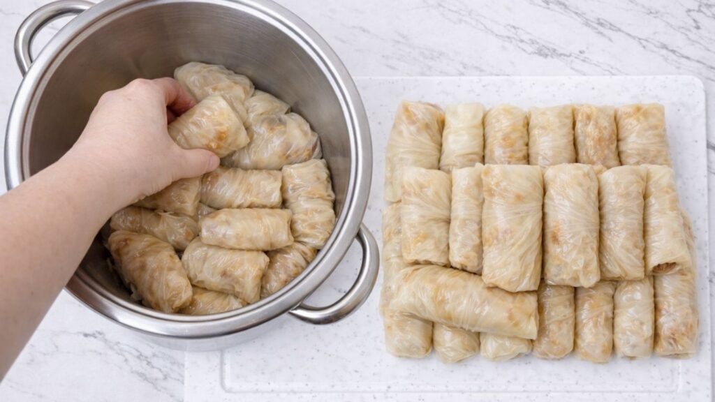 Placing rolled sarma into a pot lined with cabbage leaves, arranging the stuffed sour cabbage rolls layer by layer for cooking