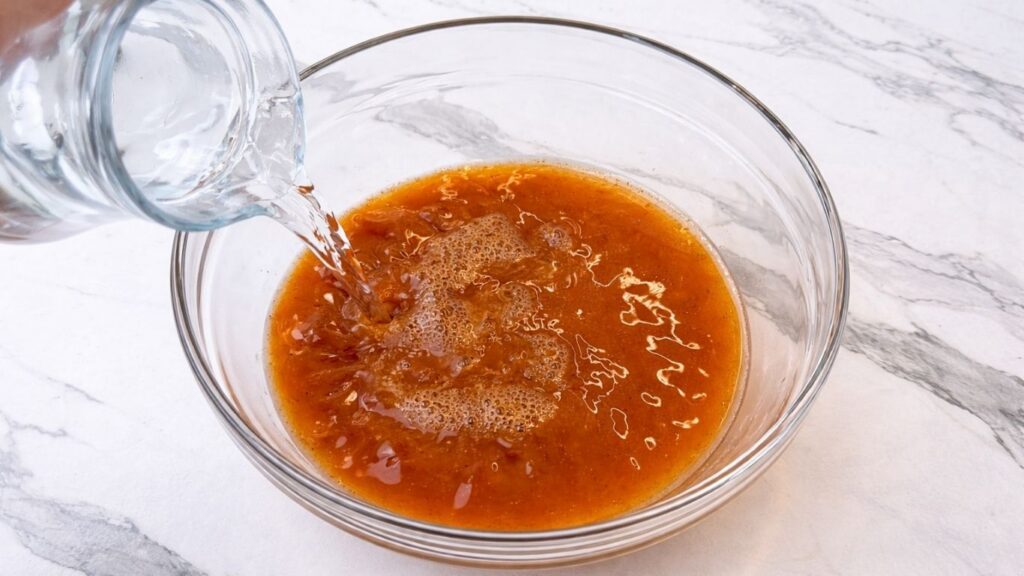 Mixing spices with water for the sarma cooking liquid and pouring in additional water to prepare the seasoned sauce for stuffed sour cabbage rolls