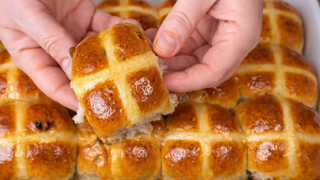 Soft and fluffy hot cross buns with golden tops and white crosses on top, freshly baked and served warm on a wooden tray