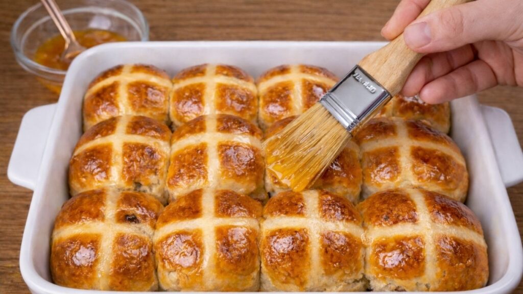 Brushing warm hot cross buns with apricot jam glaze to give them a shiny golden finish