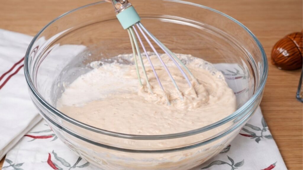 Glass bowl with activated yeast soaking in milk and sugar, foamy and risen on top, showing that the yeast is fully proofed and ready for baking dough burger buns 
