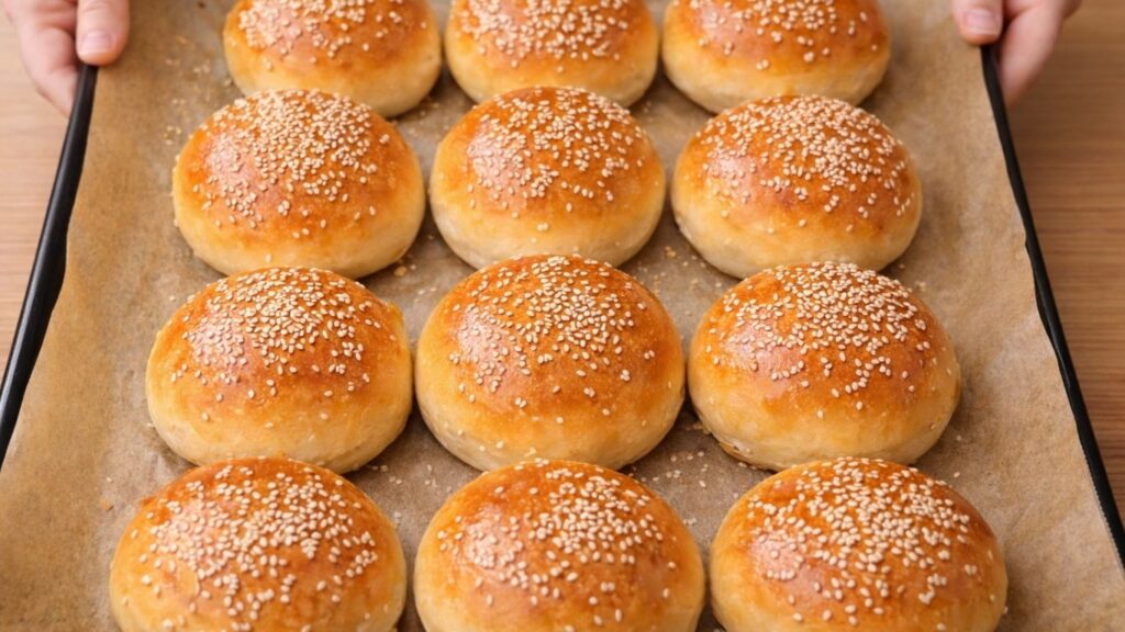 Freshly baked burger buns in a baking tray, beautifully golden on top with a soft, fluffy texture and a light glossy finish