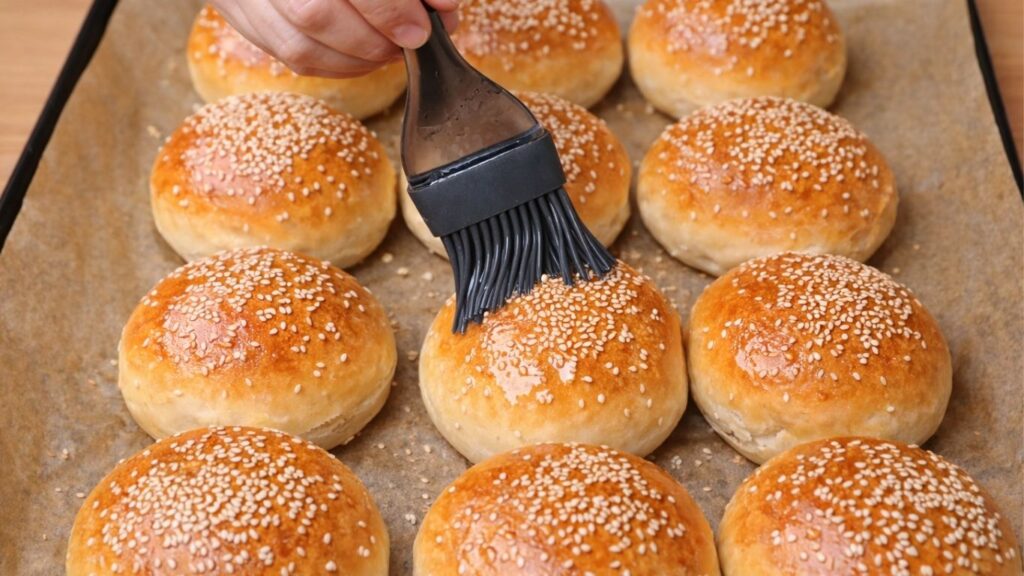 Brushing freshly baked burger buns with a light mixture of water and oil, giving them a soft, tender crust and a gentle glossy shine