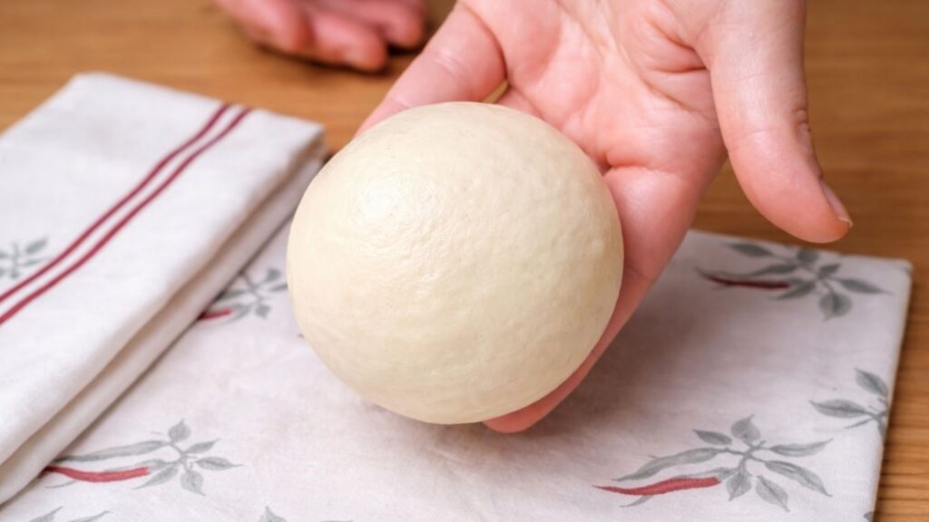 Smoothly shaped dough ball resting in my hand, soft and round, ready to be placed on the baking tray for the final rise