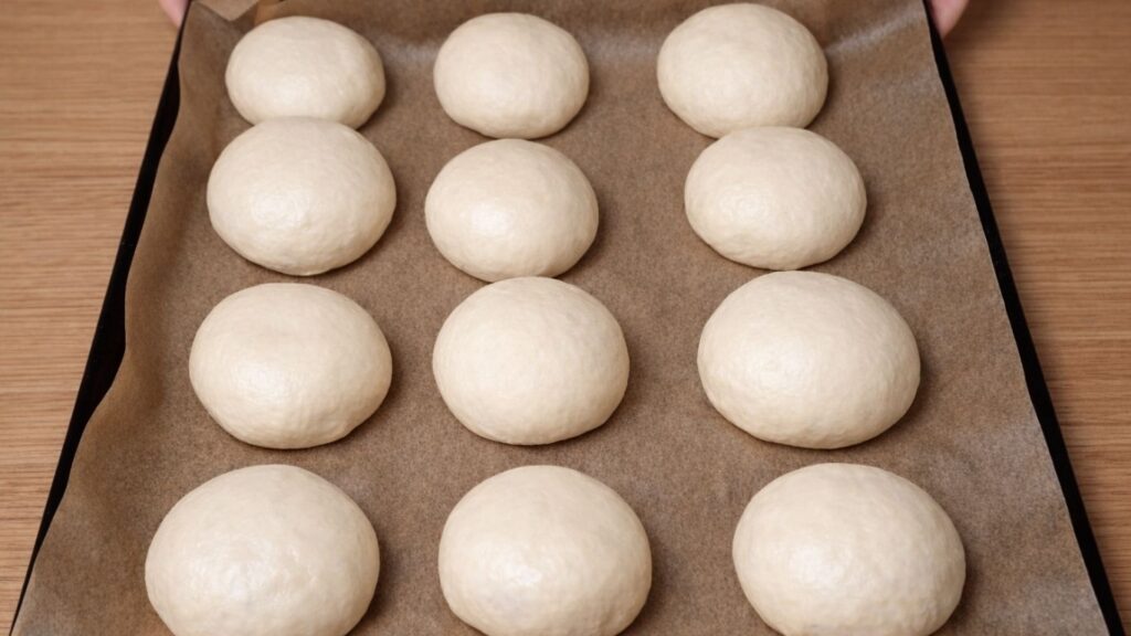 Shaped dough balls arranged on a baking tray lined with parchment paper, evenly spaced and ready for their final rise before baking