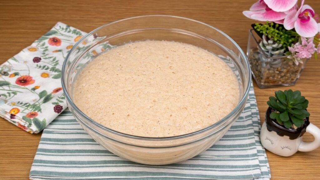 Activated yeast in a glass bowl, foamy and bubbly on the surface, showing the yeast has risen and is ready for baking, clean and natural close-up baking scene