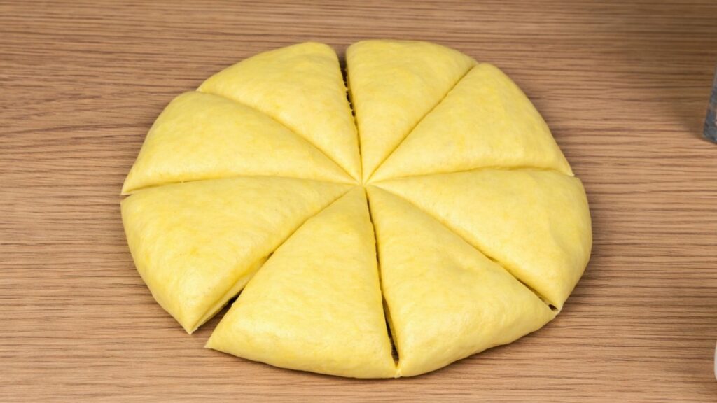Yellow dough on a clean work surface divided into eight equal portions, ready to be shaped into burger buns, smooth and soft texture, natural baking preparation scene