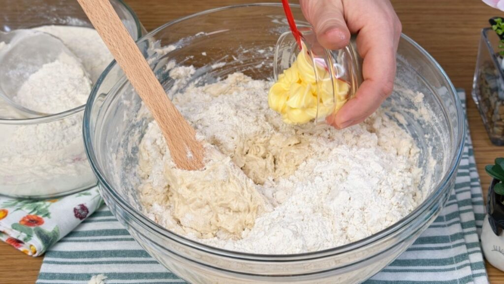 Glass bowl with activated yeast mixture combined with flour, salt, and butter, ingredients being added together to form the dough, clean and natural baking preparation scene