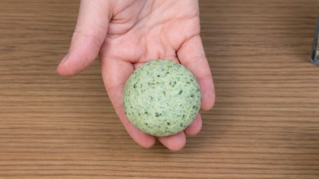 Green dough ball held in hand, smooth and elastic texture, ready for shaping into burger buns, clean and natural baking preparation scene