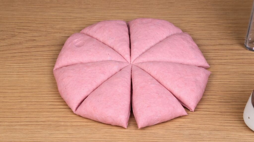 Pink dough on a clean work surface divided into eight equal portions, smooth and soft pieces ready to be shaped into burger buns, natural baking preparation scene