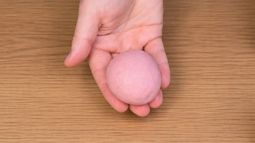 Pink dough shaped into a smooth round ball, soft and elastic texture ready for proofing, natural baking preparation scene