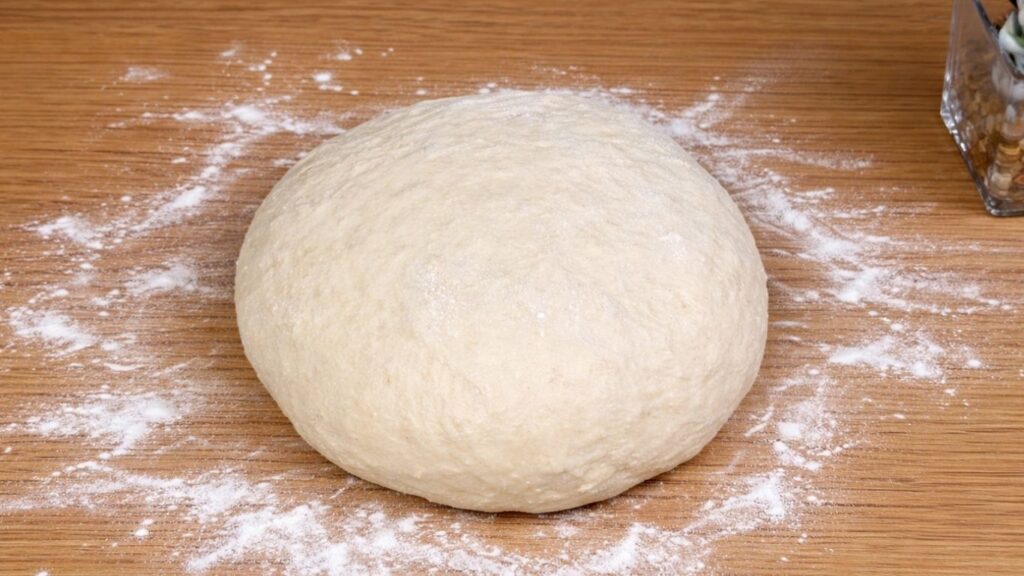 Kneaded dough resting on a clean work surface, smooth, soft and elastic texture ready for shaping, natural light and homemade baking scene