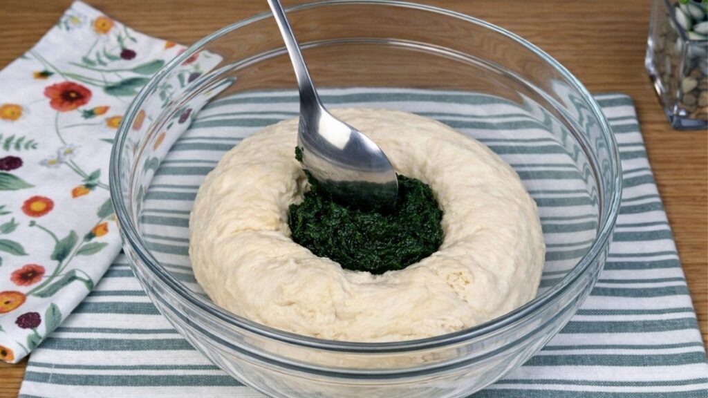 Glass bowl with a portion of dough as blended spinach is being added to color it naturally green, close-up clean baking preparation scene