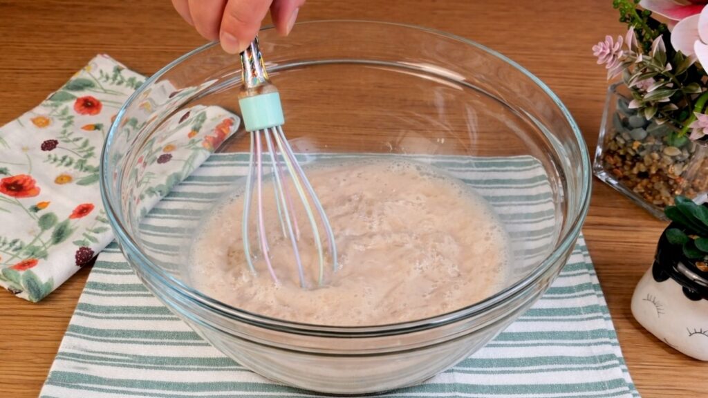 Mixing yeast, warm water and sugar in a glass bowl to activate the yeast for pretzel buns dough.