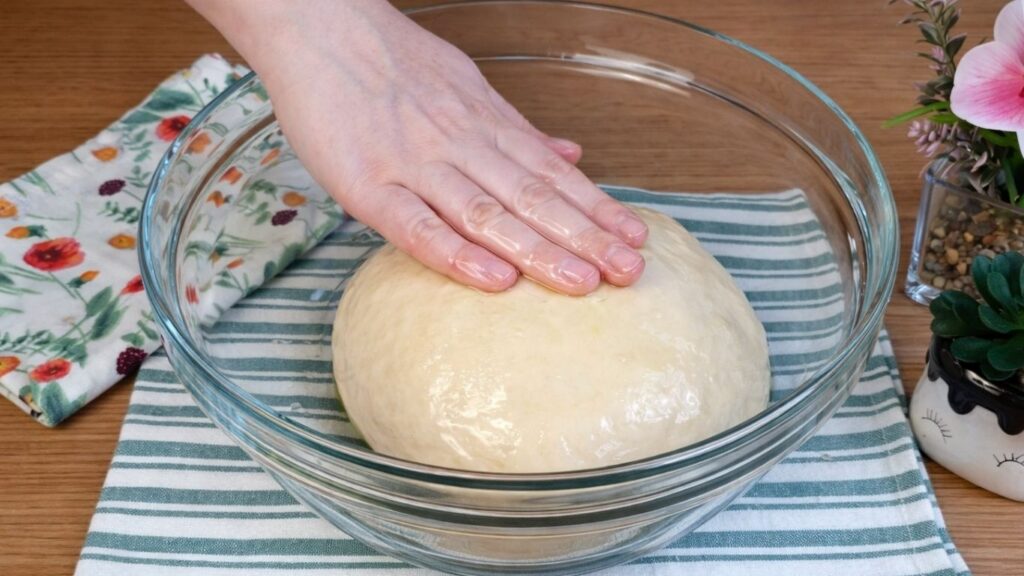Smooth pretzel buns dough in a bowl lightly brushed with oil, ready for rising.