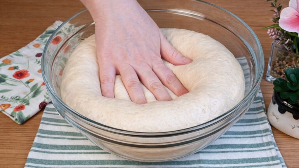 Risen pretzel buns dough gently pressed by hand to show how soft, airy and well risen it is.