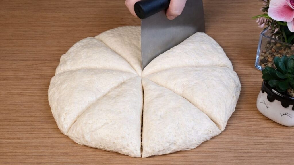Pretzel buns dough on a wooden surface divided into 8 equal pieces, ready for shaping.