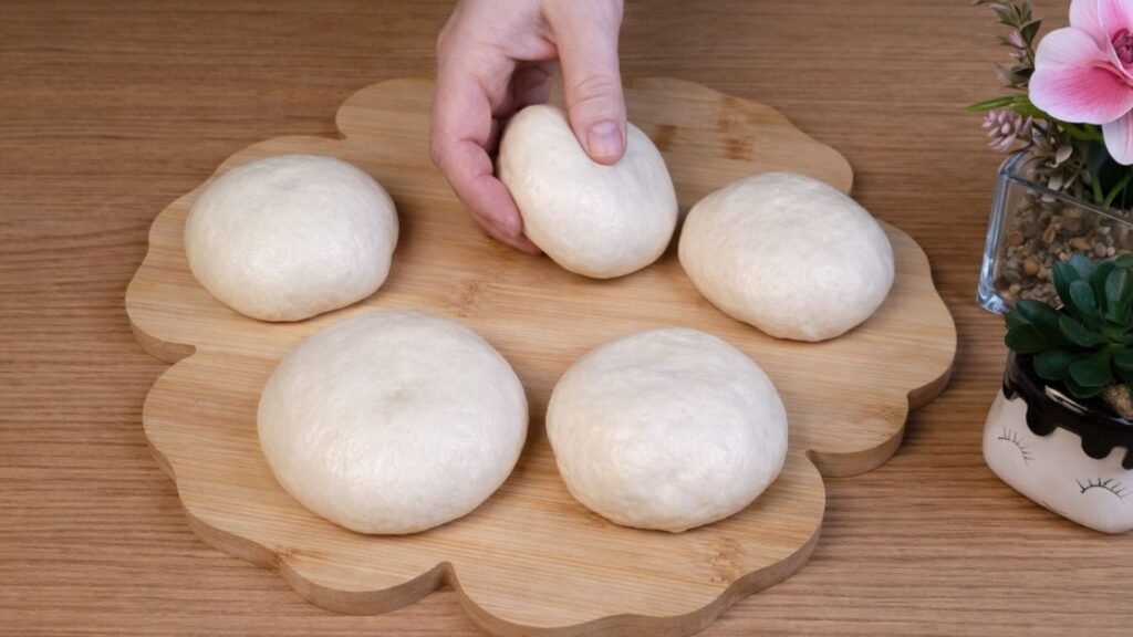 Shaped pretzel buns dough balls arranged on a wooden board, ready for the next step.