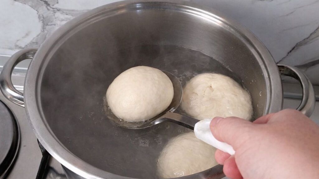 Placing shaped pretzel buns dough into boiling water with baking soda for the classic pretzel bath.