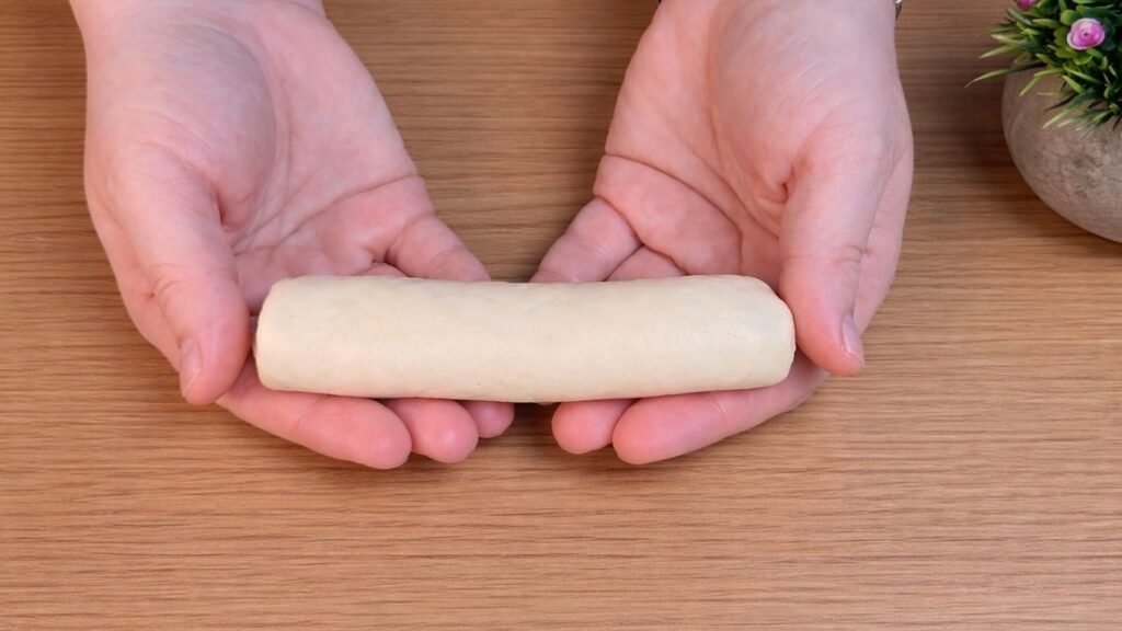 Hand holding a freshly shaped homemade hot dog bun before placing it on the baking tray.