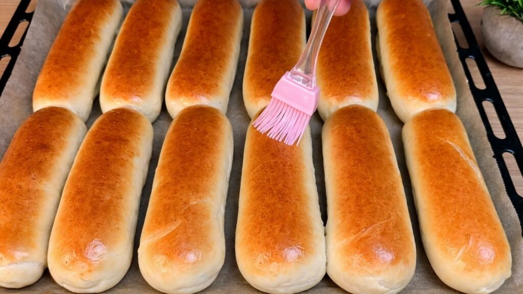 Brushing warm homemade hot dog buns with a mixture of water and oil after baking.