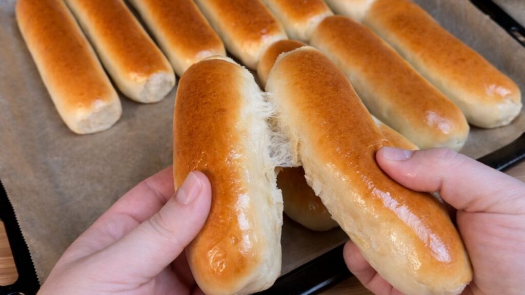 Pulling apart two freshly baked homemade hot dog buns by hand to show the soft interior.