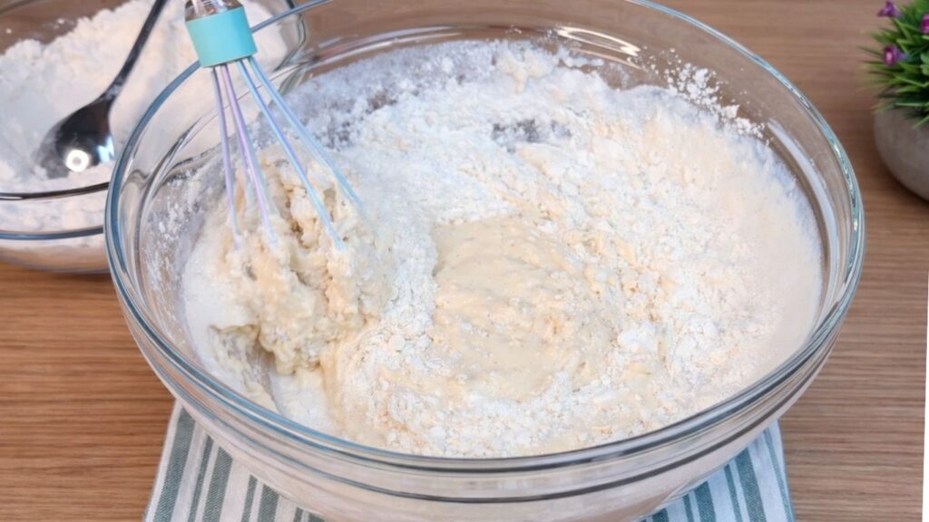 Adding flour to the wet ingredients and mixing the dough for homemade hot dog buns.