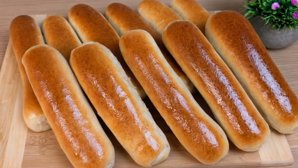 Freshly baked homemade hot dog buns arranged on a wooden board.