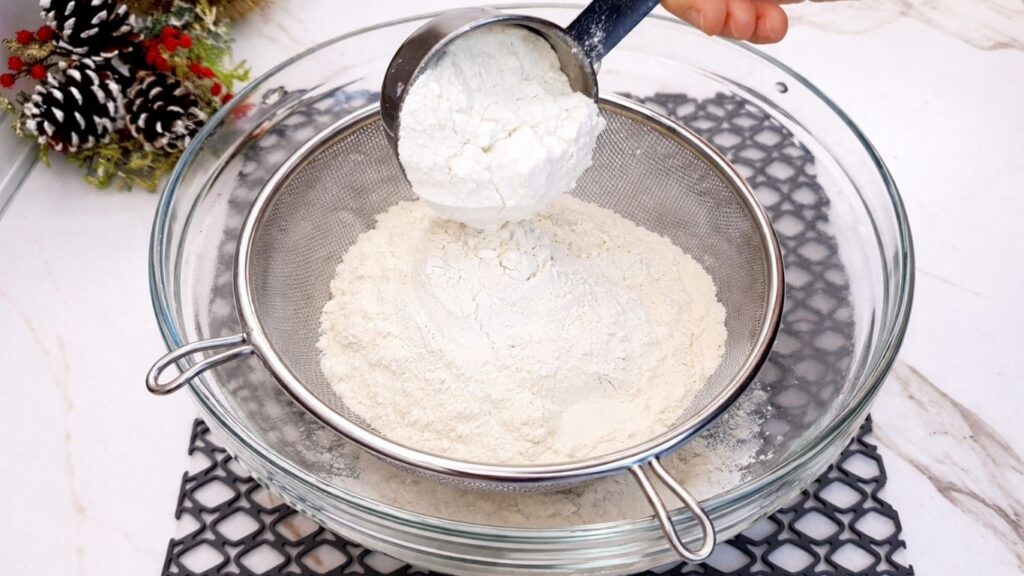 sifting flour into activated yeast mixture for soft homemade dinner rolls