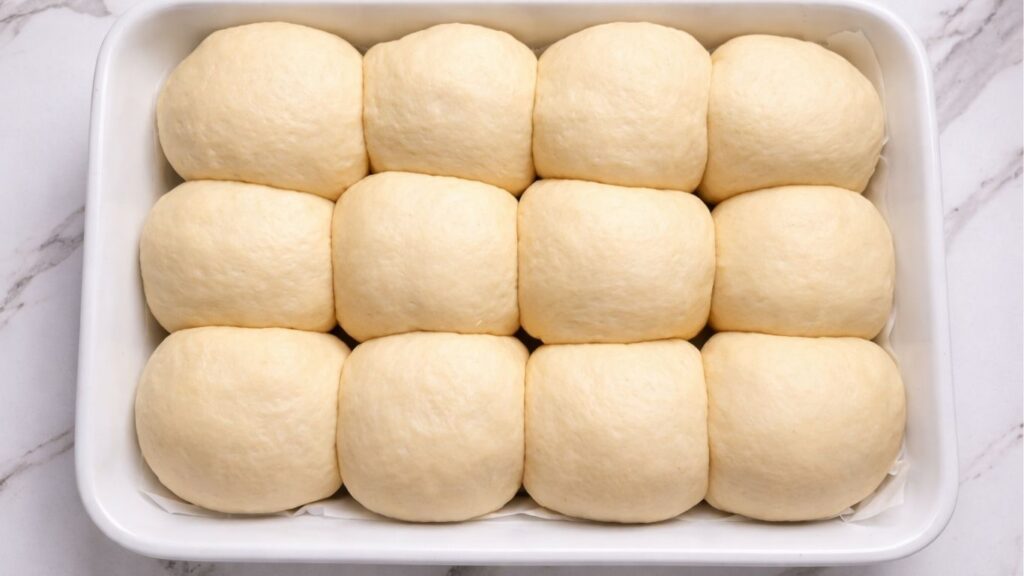 risen dough balls in the baking tray ready to bake for soft homemade dinner rolls