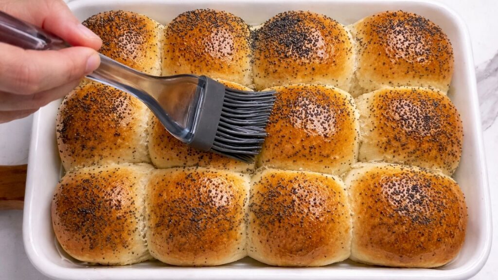 brushing melted butter over warm dinner rolls in the baking tray