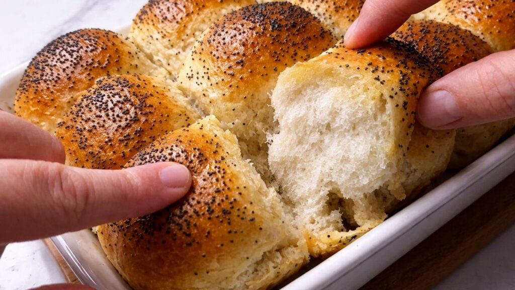pulling apart soft dinner rolls with both hands in the baking tray showing fluffy texture