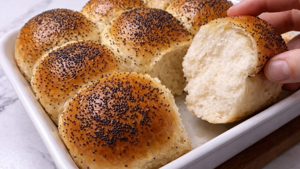 hand pulling apart one soft dinner roll in the baking tray showing fluffy interior