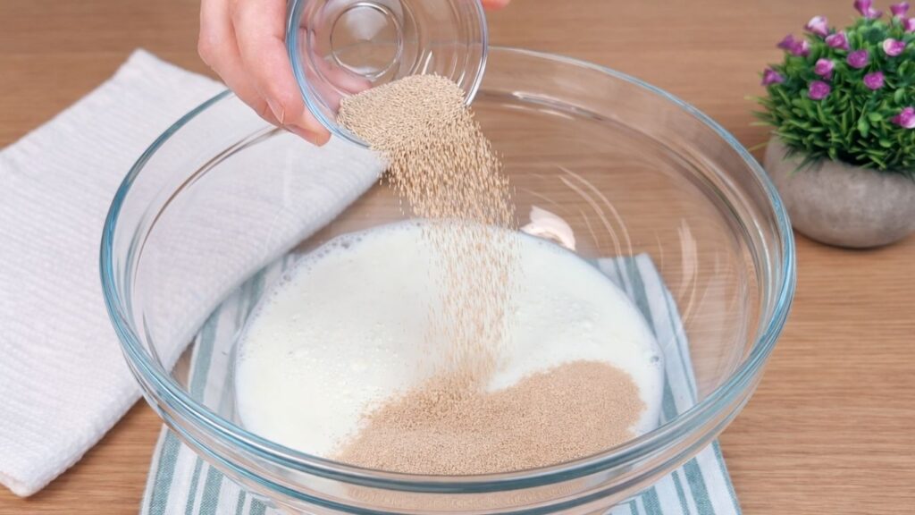 Active dry yeast being added to warm milk to activate the dough for homemade hot dog buns.