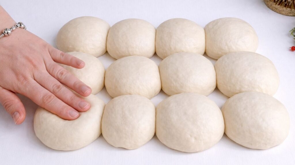 Pressing risen dough balls by hand before shaping baguettes