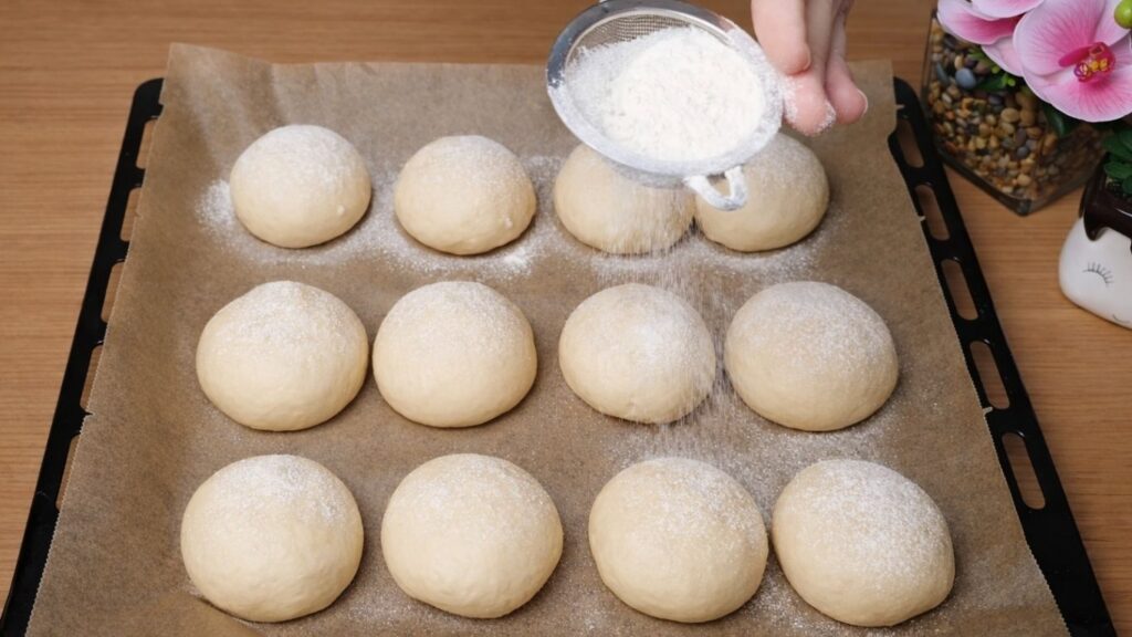 Shaped dough balls arranged in a baking tray and lightly dusted with flour before baking in this Easy Milk Buns Recipe.