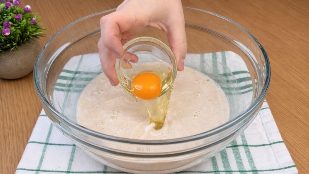 adding egg to the activated yeast mixture while preparing dough for blueberry lemon rolls