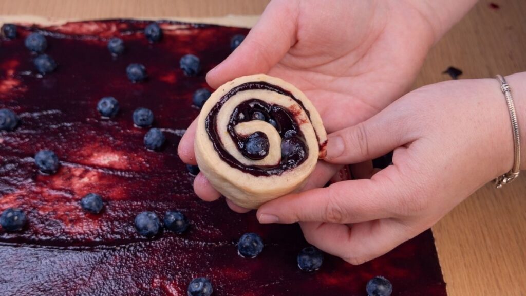 holding a shaped blueberry lemon roll in hand ready to place in the baking pan