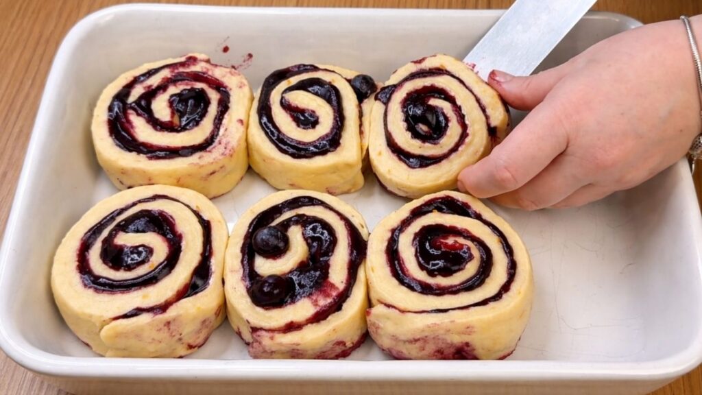 shaped blueberry lemon rolls arranged in a baking pan ready for baking