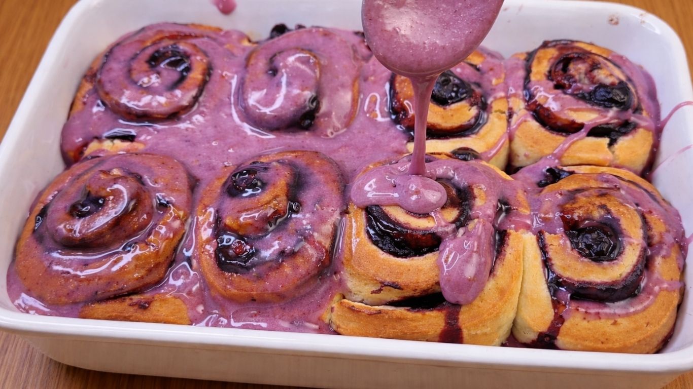 freshly baked blueberry lemon rolls in a baking pan topped with creamy cream cheese frosting
